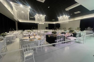 Salle de réception décorée avec des chaises blanches alignées et des arrangements floraux, prête pour un événement.