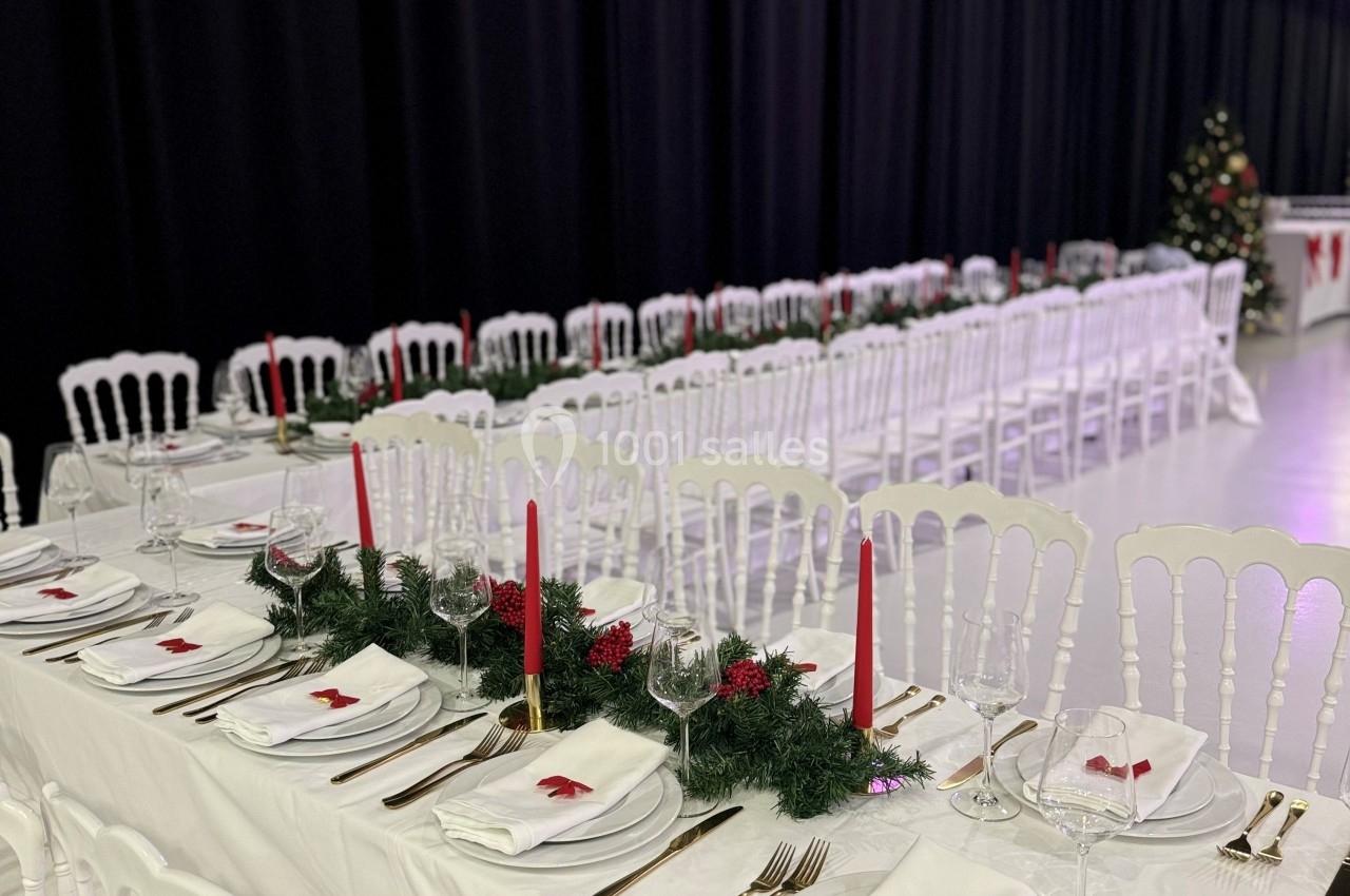 Tables de banquet décorées avec nappes blanches, bougies rouges, couverts dorés et guirlandes de sapin.