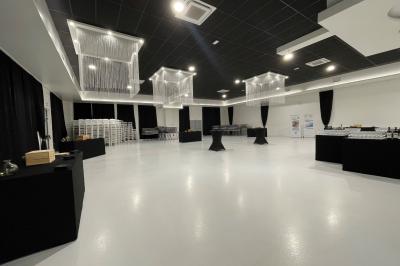 Salle de réception décorée avec des chaises blanches alignées et des arrangements floraux, prête pour un événement.