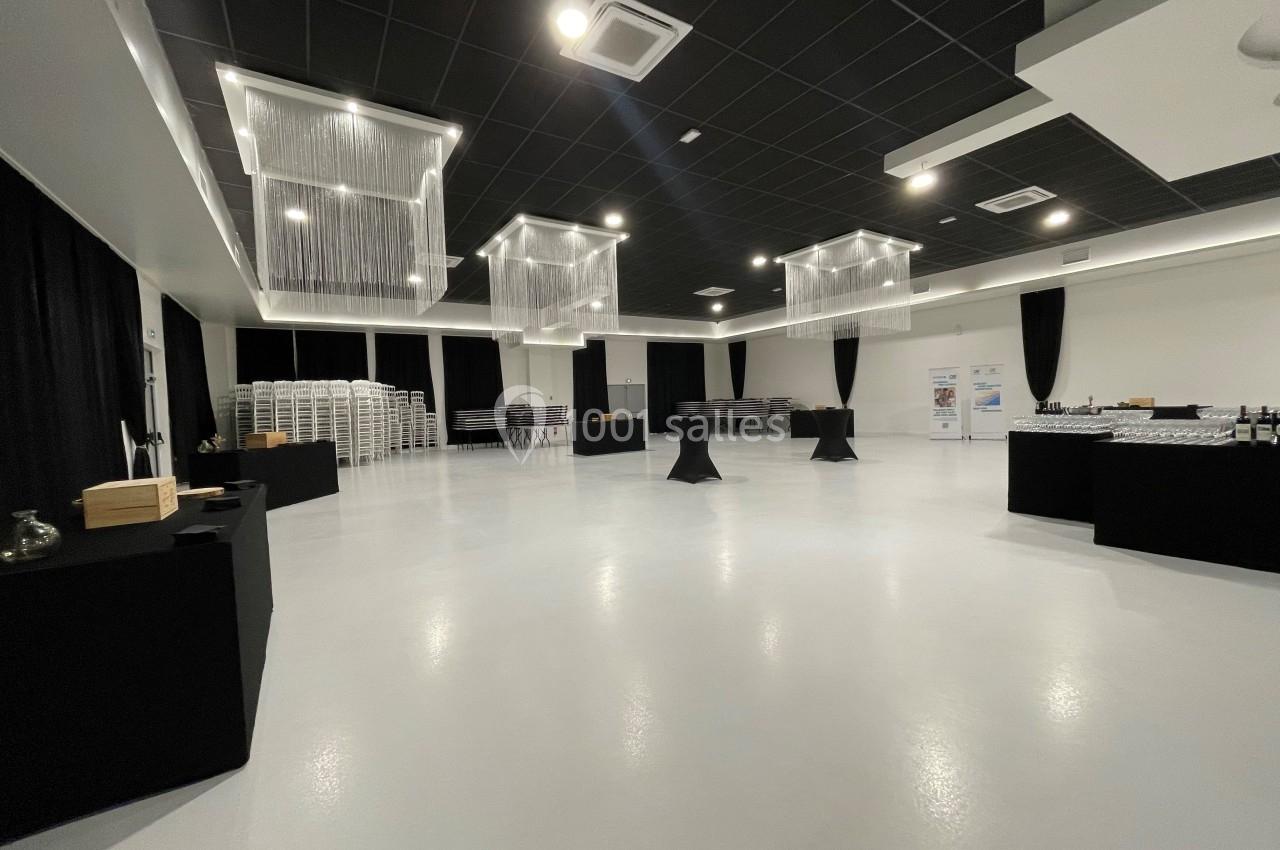 Salle spacieuse avec tables hautes, nappes noires, chaises empilées et éclairage moderne suspendu.