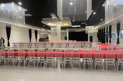 Salle de réception décorée avec des chaises blanches alignées et des arrangements floraux, prête pour un événement.