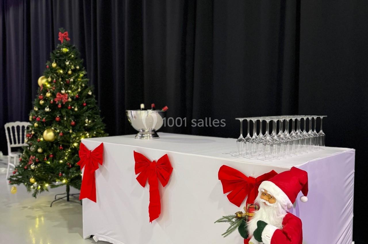 Table décorée avec des rubans rouges, un Père Noël miniature, un sapin de Noël illuminé et des flûtes à champagne.