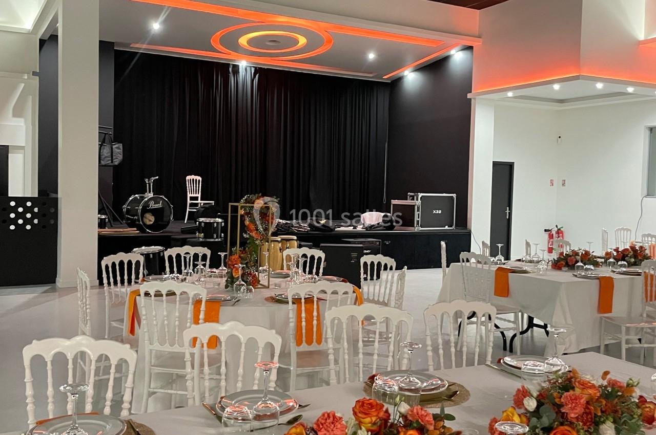 Salle de réception décorée avec des tables dressées, des chaises blanches et des arrangements floraux orange devant une…