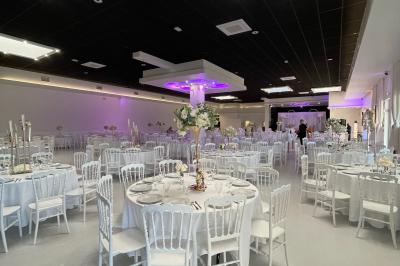 Salle de réception décorée avec des chaises blanches alignées et des arrangements floraux, prête pour un événement.