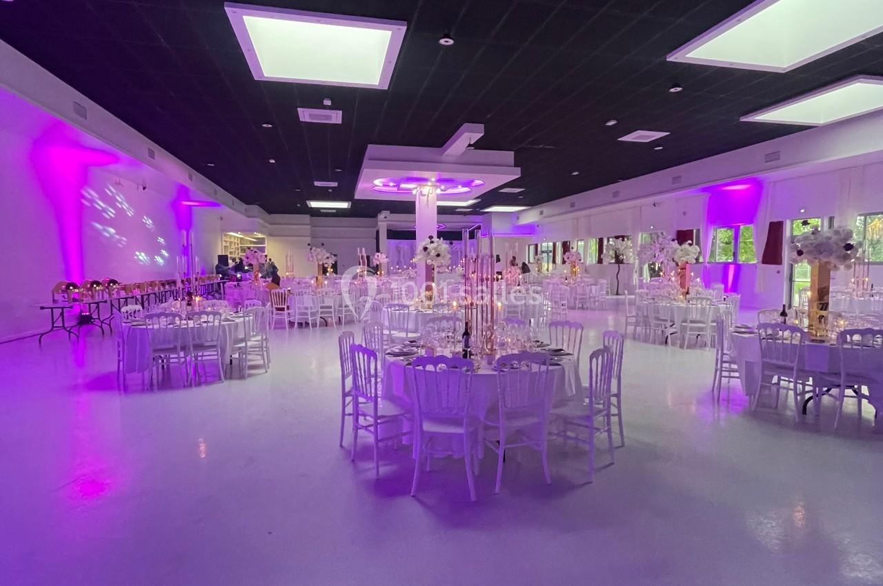 Salle de réception spacieuse avec tables rondes décorées, éclairage violet et plafond noir avec lumières intégrées.