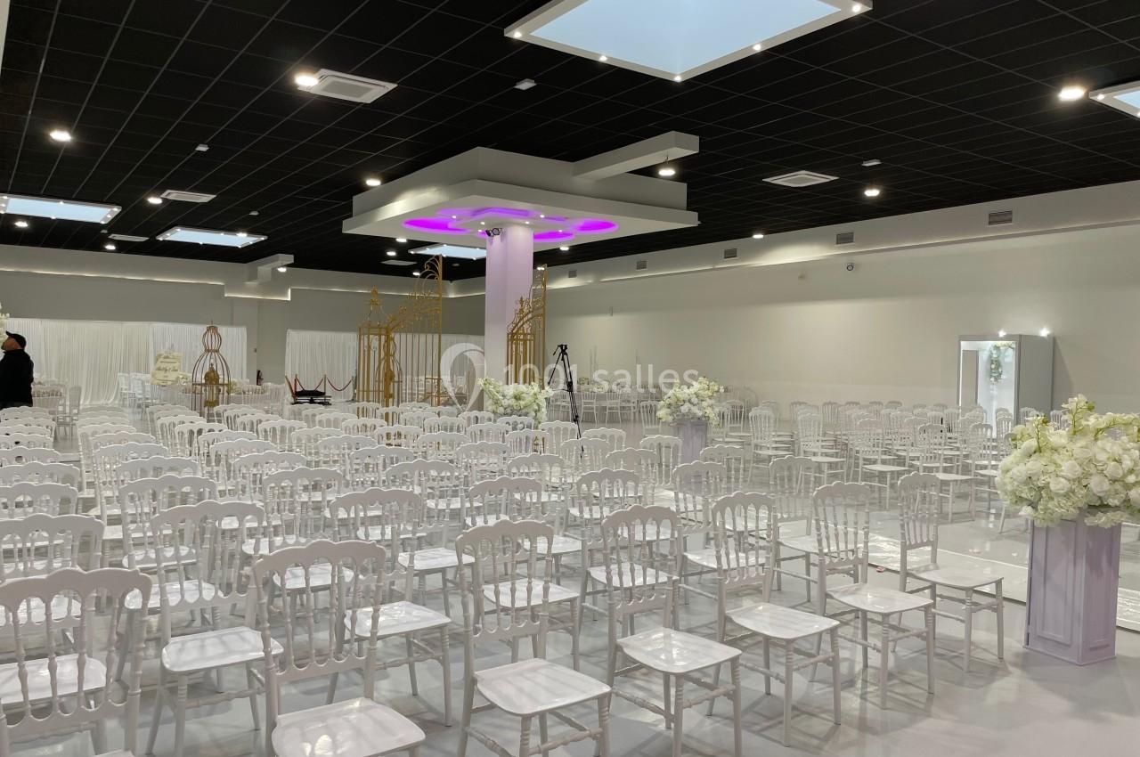 Salle de réception décorée avec des chaises blanches alignées et des arrangements floraux, prête pour un événement.