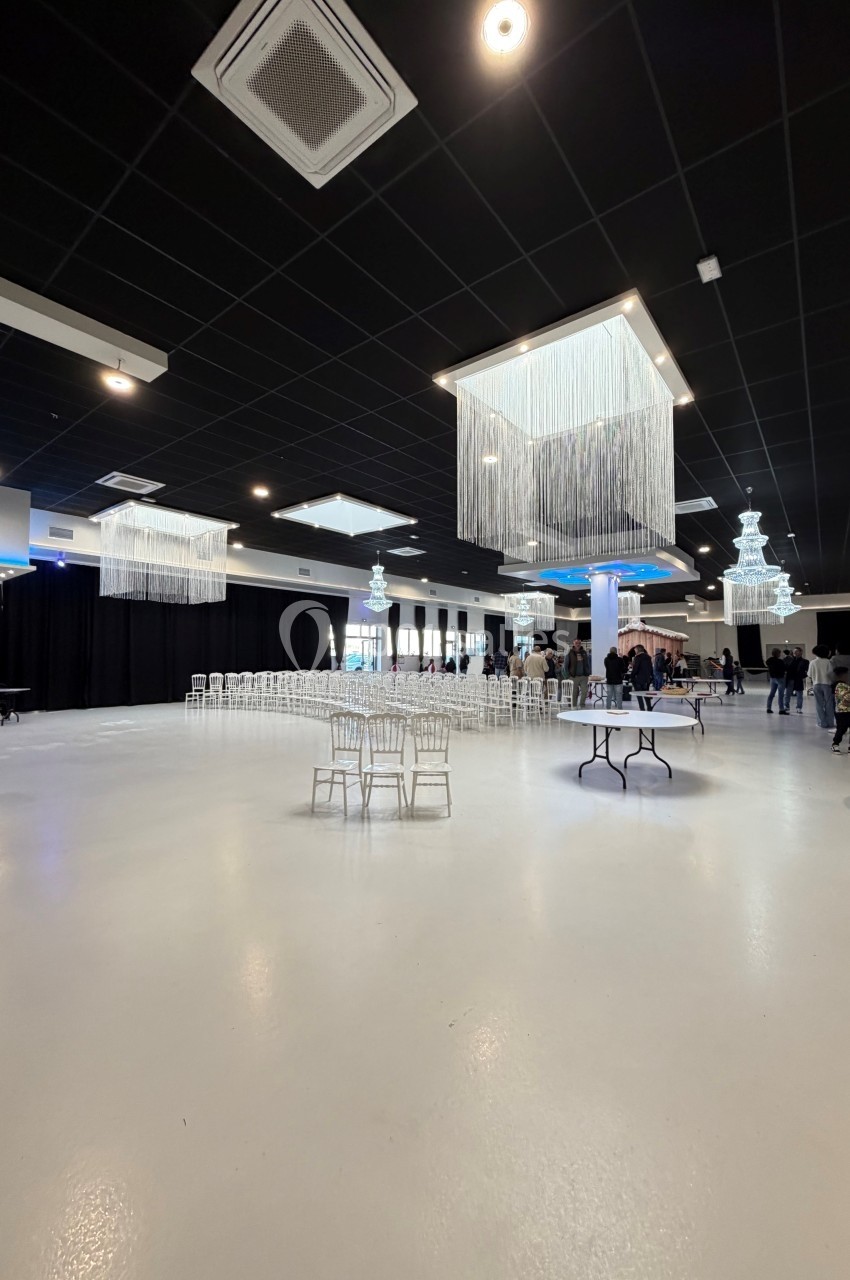 Salle spacieuse avec sol blanc, plafond noir, lustres modernes et chaises disposées pour un événement.