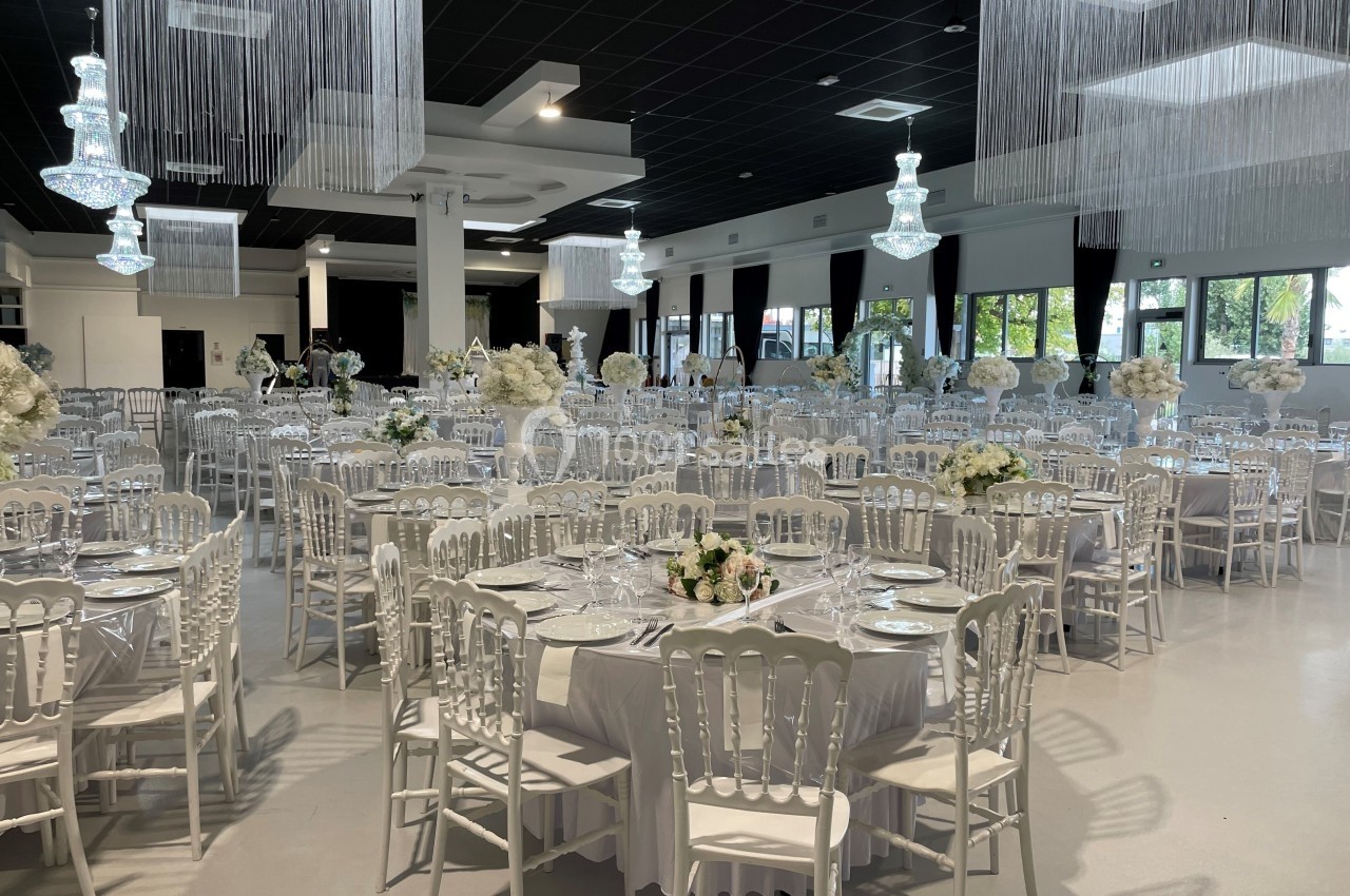 Salle de réception élégante avec tables rondes décorées de nappes blanches, chaises assorties et lustres suspendus.