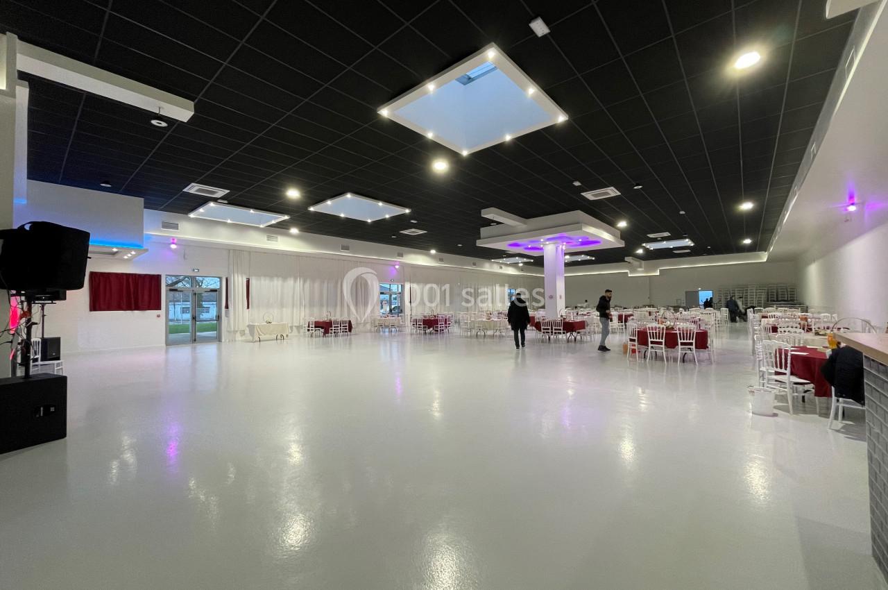 Salle spacieuse avec sol brillant, tables dressées et éclairage moderne, quelques personnes en arrière-plan.