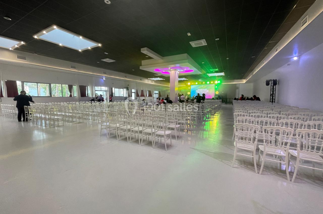Salle spacieuse avec des rangées de chaises blanches, éclairage coloré sur une scène au fond.