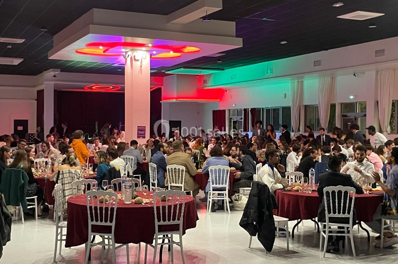 Salle remplie de personnes assises à des tables rondes, lors d'un événement ou d'un repas collectif.