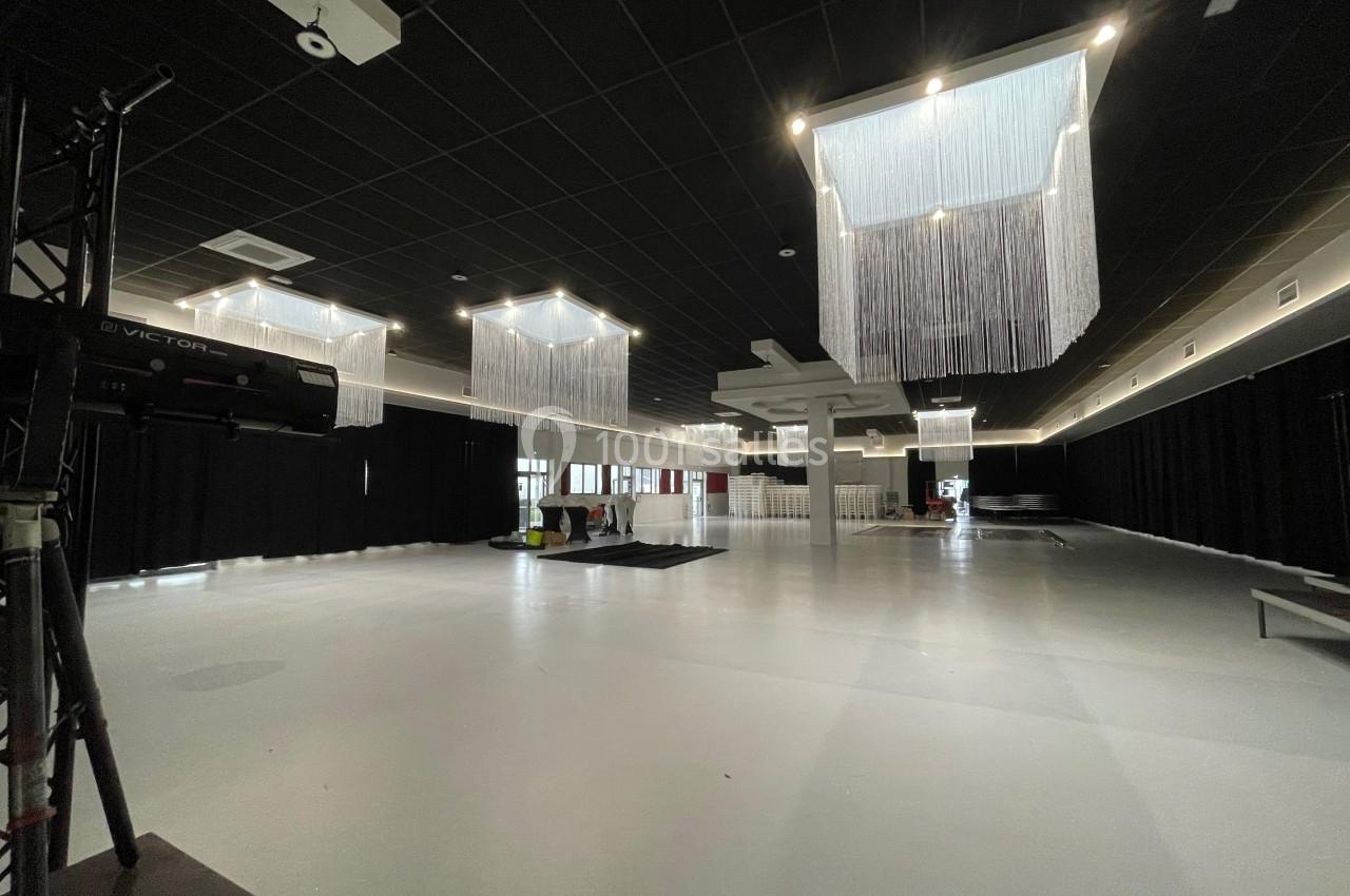 Salle spacieuse avec sol clair, plafond noir, rideaux sombres et luminaires suspendus en fils lumineux.