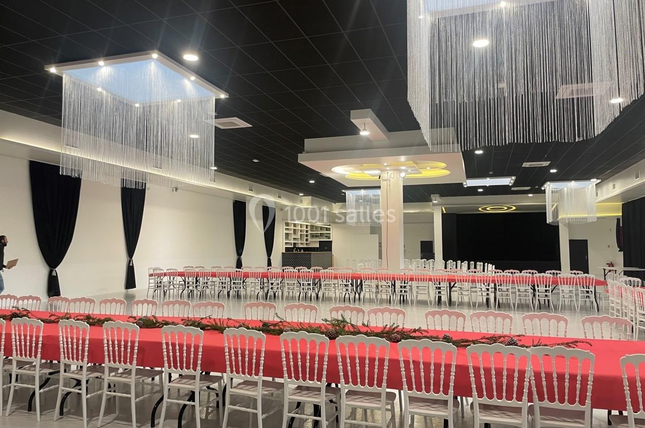 Salle de réception moderne avec tables rectangulaires dressées de nappes rouges, chaises blanches et décorations suspendues.