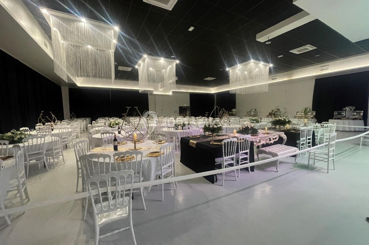 Salle de réception décorée avec des tables rondes, nappes blanches, chaises élégantes et éclairage suspendu moderne.
