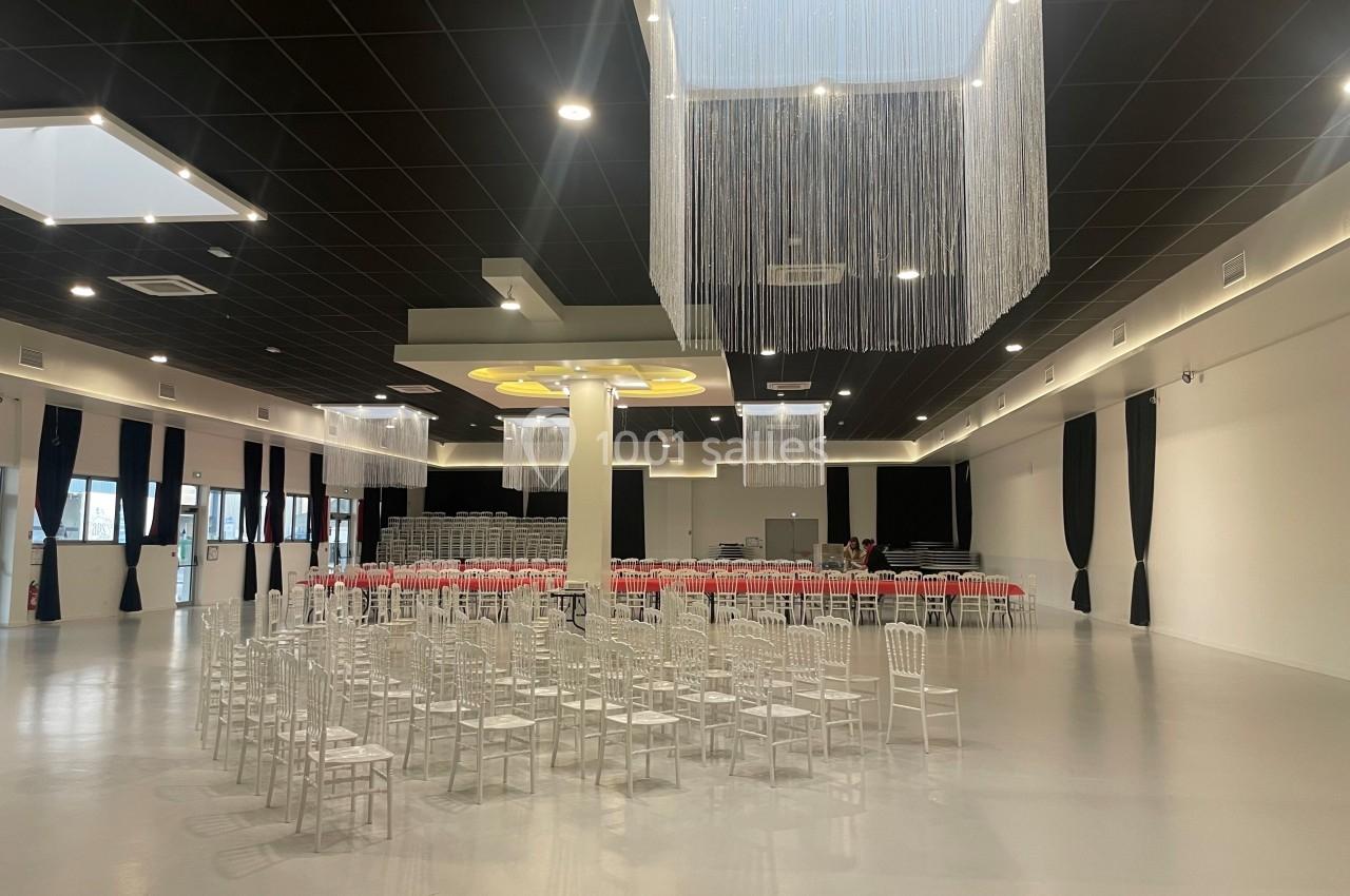Salle spacieuse avec des chaises blanches alignées, rideaux noirs, plafond moderne et éclairage suspendu.