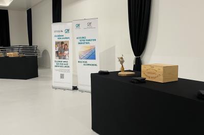 Deux roll-ups promotionnels et une table noire avec des boîtes en bois dans une salle lumineuse au sol blanc.