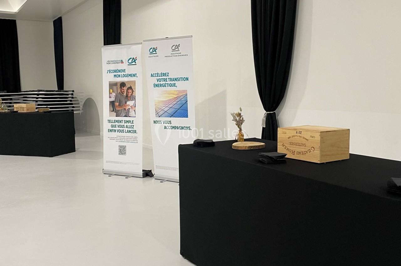 Deux roll-ups promotionnels et une table noire avec des boîtes en bois dans une salle lumineuse au sol blanc.