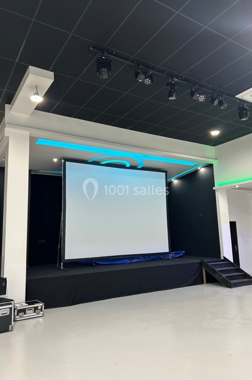 Scène avec écran de projection blanc, éclairage LED bleu et noir, située dans une salle moderne avec sol clair.