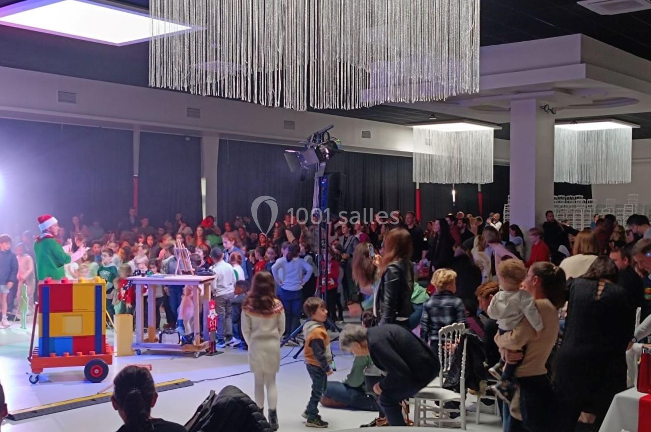Un spectacle pour enfants avec un animateur déguisé en Père Noël, entouré d'un public dans une salle décorée.