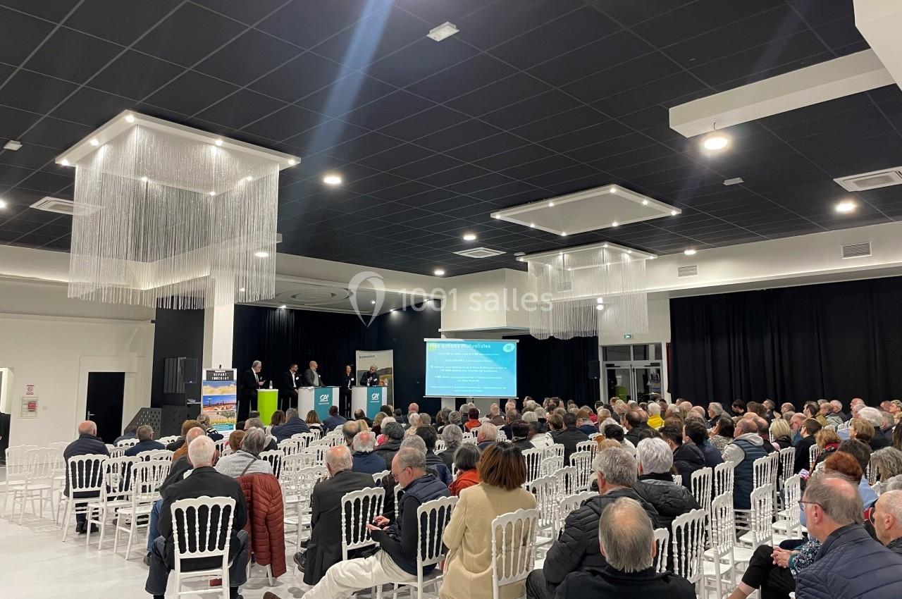 Salle de conférence avec un public assis écoutant des intervenants sur une scène devant un écran de présentation.