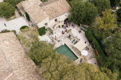 Vue aérienne d'une grande maison en pierre avec piscine, entourée de forêts et de champs sous un ciel dégagé.
