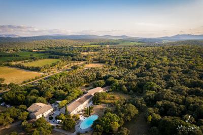 Vue aérienne d'une grande maison en pierre avec piscine, entourée de forêts et de champs sous un ciel dégagé.