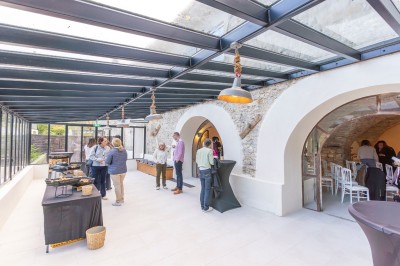 Vue aérienne d'une grande maison en pierre avec piscine, entourée de forêts et de champs sous un ciel dégagé.