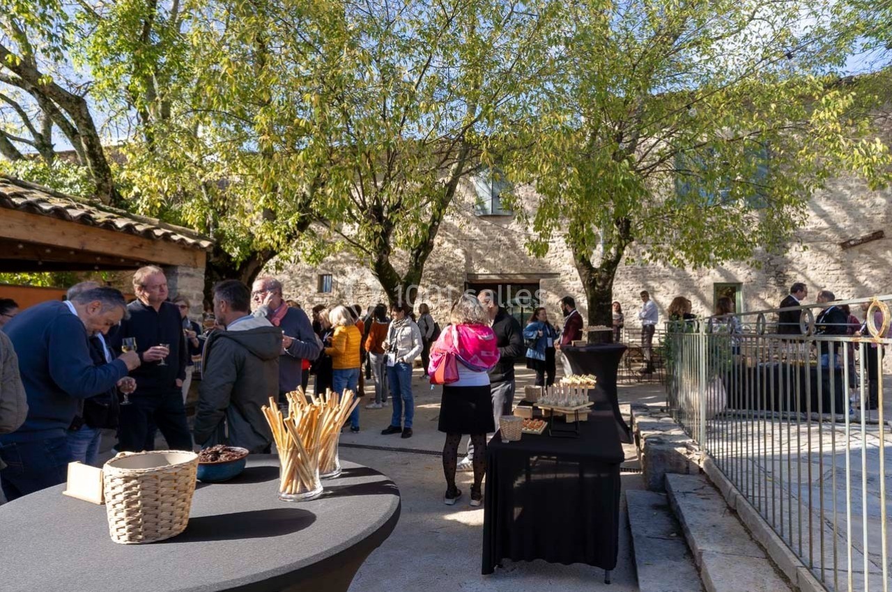 Personnes rassemblées dans une cour extérieure ensoleillée, discutant près de tables avec des collations.