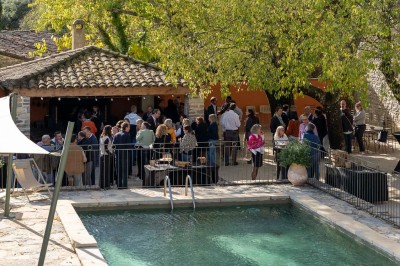 Vue aérienne d'une grande maison en pierre avec piscine, entourée de forêts et de champs sous un ciel dégagé.