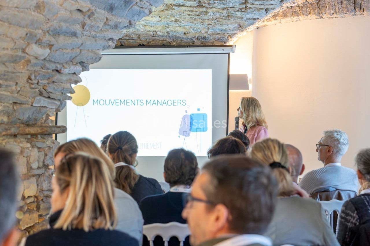 Une femme présente un diaporama devant un public assis dans une salle voûtée en pierre.