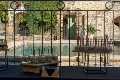 Vue aérienne d'une grande maison en pierre avec piscine, entourée de forêts et de champs sous un ciel dégagé.