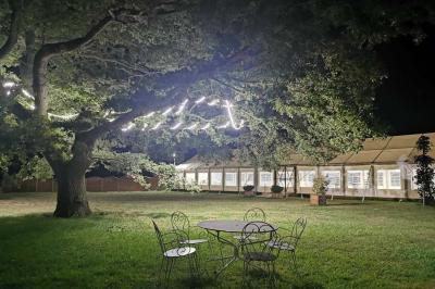 Un grand arbre illuminé par des guirlandes lumineuses dans un jardin avec des tables et chaises en soirée.