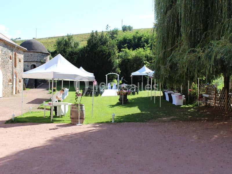 Espace extérieur aménagé pour un événement avec tentes blanches, chaises et décorations florales sur une pelouse.