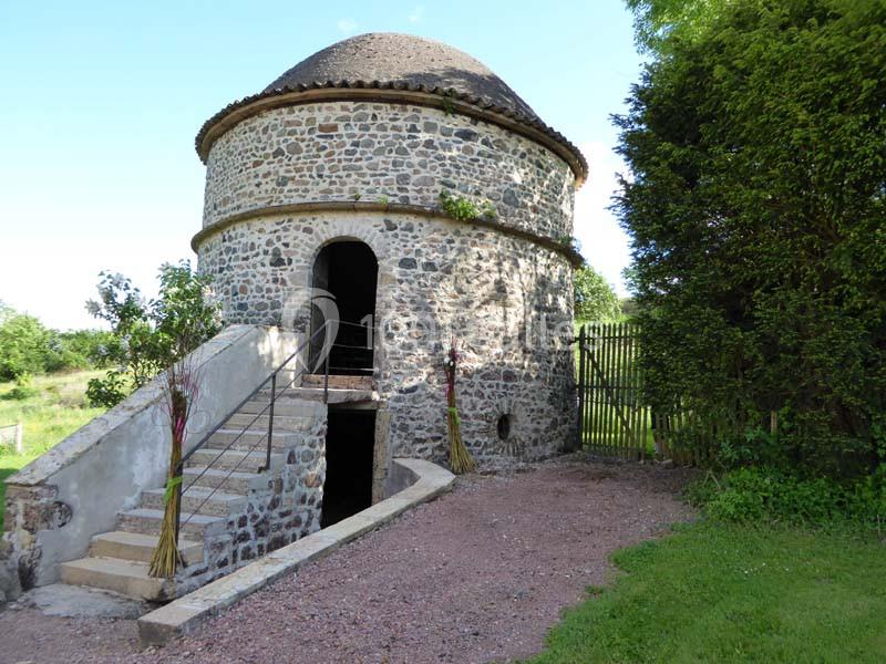 Bâtiment circulaire en pierre avec un toit en dôme, escalier extérieur et végétation environnante.