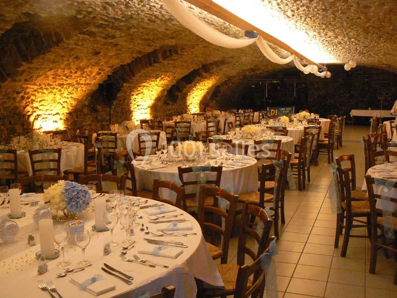 Salle voûtée en pierre aménagée pour un banquet, avec tables rondes dressées et décorations lumineuses chaleureuses.