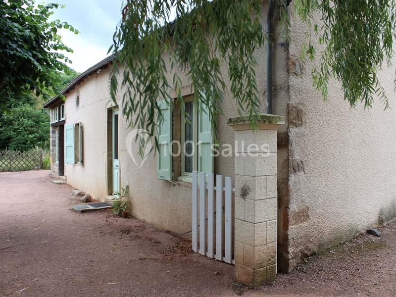 Maison en pierre avec volets verts, petite clôture blanche et végétation environnante.
