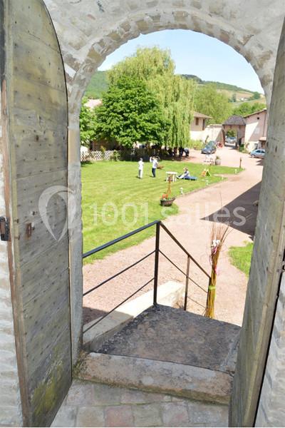 Vue depuis une porte en pierre ouverte donnant sur une cour verdoyante avec des personnes et des arbres en arrière-plan.