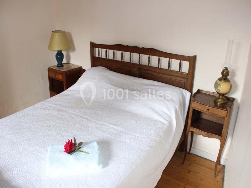 Lit double avec une couverture blanche, une serviette pliée et une fleur rouge, entouré de tables de chevet en bois.