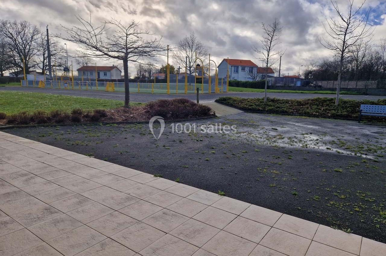 Allée pavée donnant sur un espace extérieur avec terrain de sport, pelouse, arbres et maisons en arrière-plan.