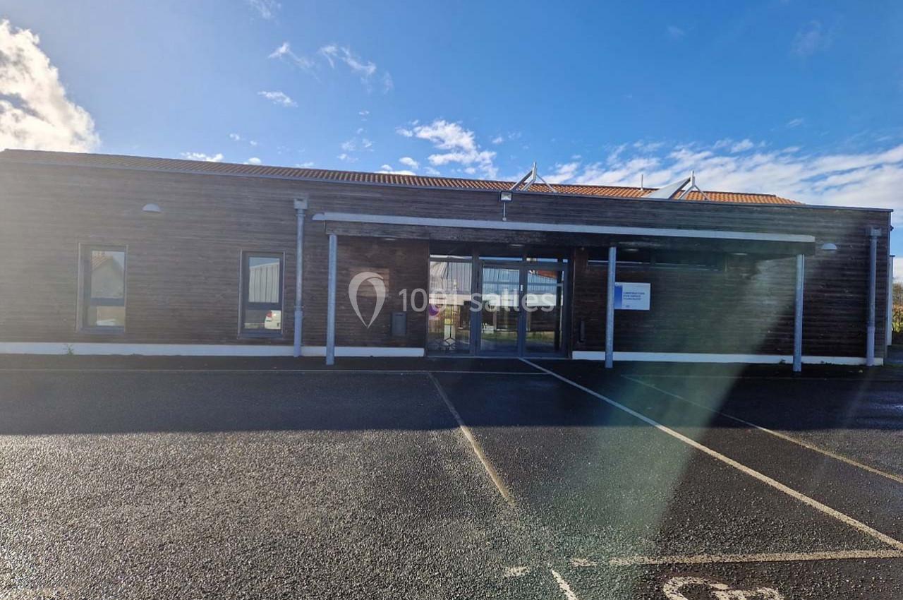 Façade d’un bâtiment moderne en bois avec une entrée vitrée, vue depuis un parking sous un ciel partiellement nuageux.