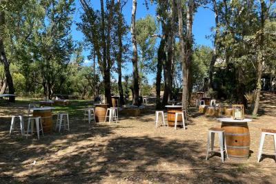 Terrasse aménagée pour un événement avec tables hautes drapées de noir, guirlandes lumineuses et végétation en arrière-plan.