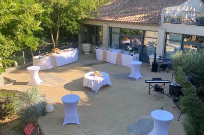 Terrasse aménagée pour un événement avec tables hautes drapées de noir, guirlandes lumineuses et végétation en arrière-plan.