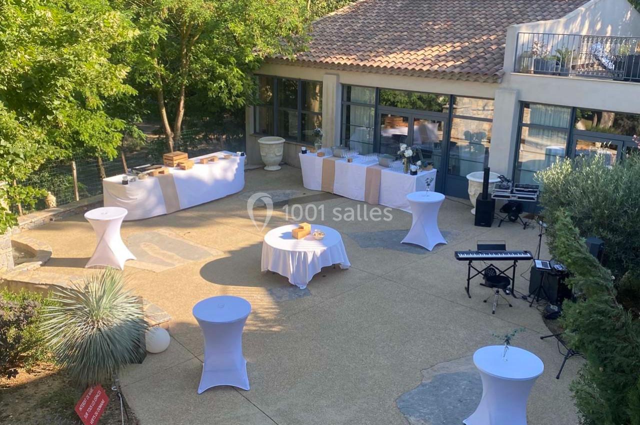 Terrasse aménagée pour un événement avec tables hautes, buffets, piano et végétation environnante.