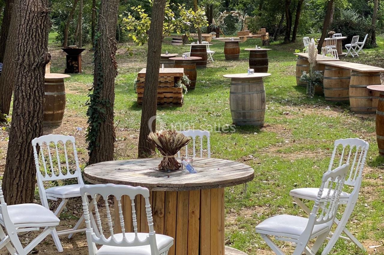 Tables et chaises en bois et en métal blanc disposées en extérieur dans un cadre boisé et verdoyant.