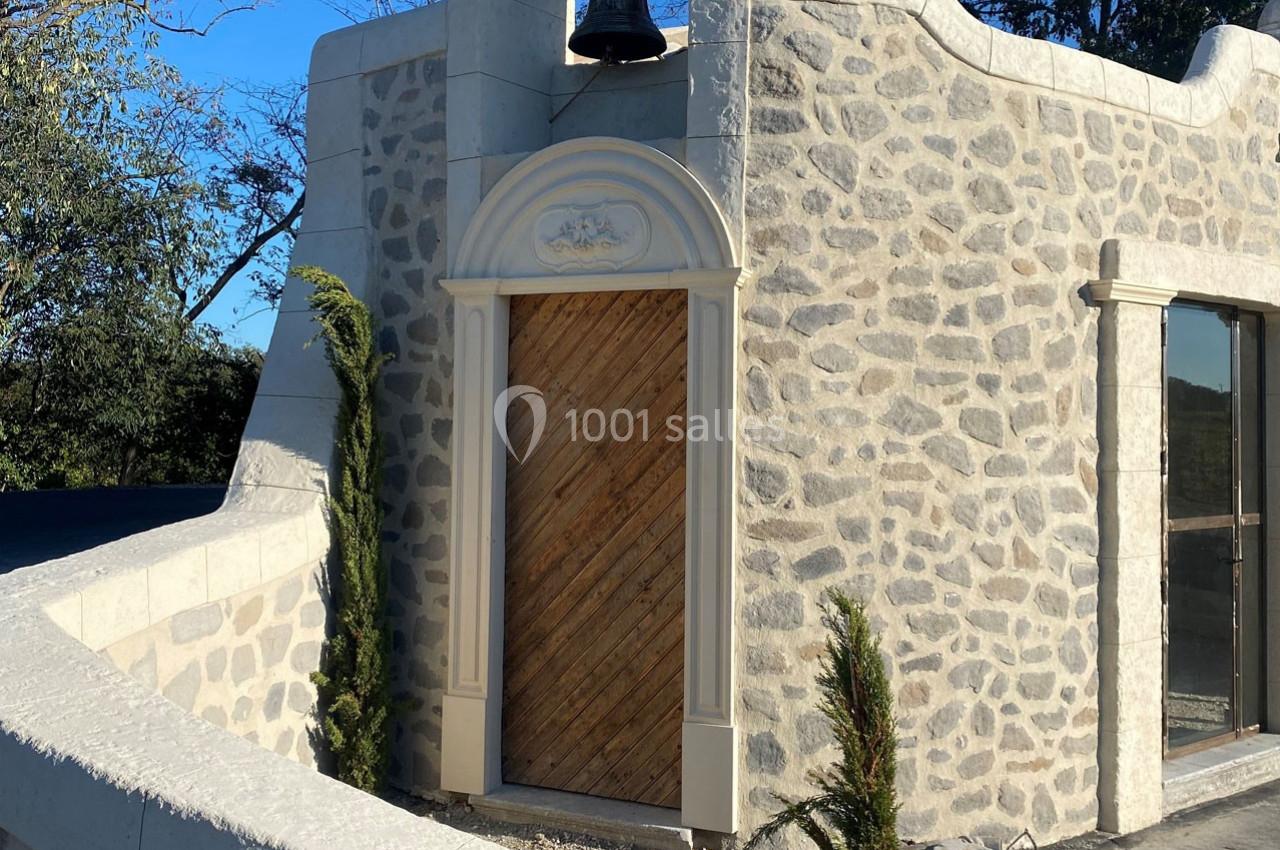 Porte en bois encadrée de pierre taillée dans un bâtiment en pierre avec un arbre et un ciel dégagé en arrière-plan.