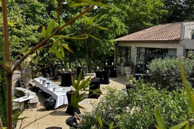 Terrasse aménagée pour un événement avec tables hautes drapées de noir, guirlandes lumineuses et végétation en arrière-plan.