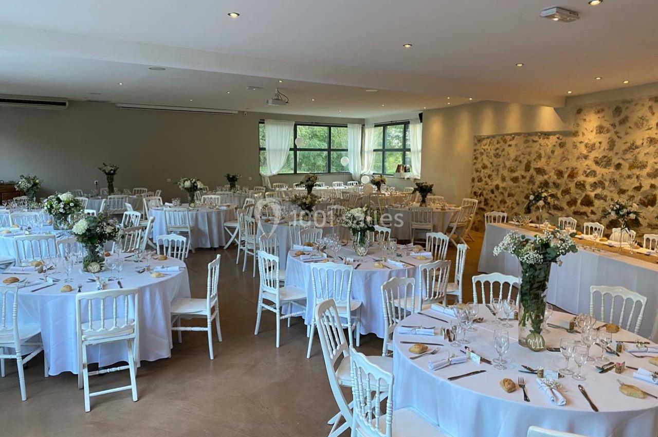 Salle de réception lumineuse avec tables rondes dressées, nappes blanches et décorations florales élégantes.