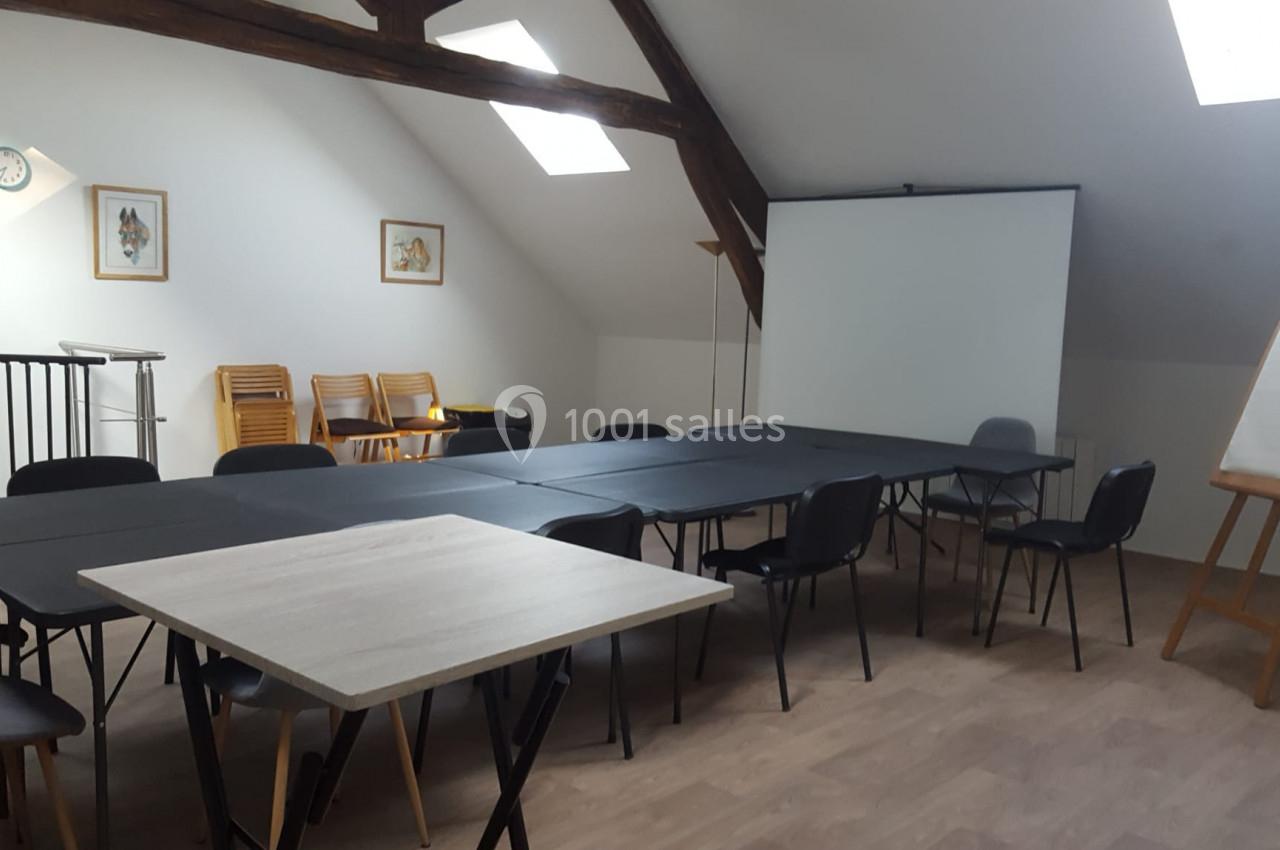 Salle de réunion avec tables noires, chaises, tableau blanc sur chevalet et écran de projection sous un toit mansardé.