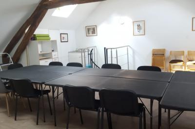 Salle de réunion avec tables noires, chaises, écran de projection, tableau blanc et éclairage naturel.