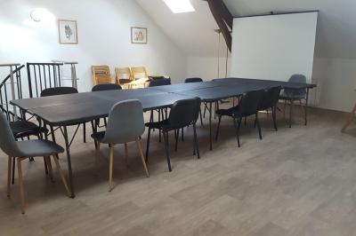 Salle de réunion avec tables noires, chaises, écran de projection, tableau blanc et éclairage naturel.